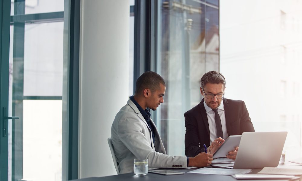 Review Your Business Life Insurance Policy Annually - Two Men Working At A Desk With A Tablet In An Office